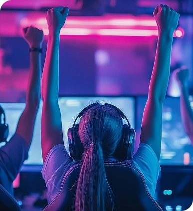 Drie gamers vieren feest in een schemerige kamer met roze en blauwe neonverlichting. Ze dragen een koptelefoon en steken hun armen in de lucht als teken van overwinning, terwijl ze naar hun beeldschermen kijken.